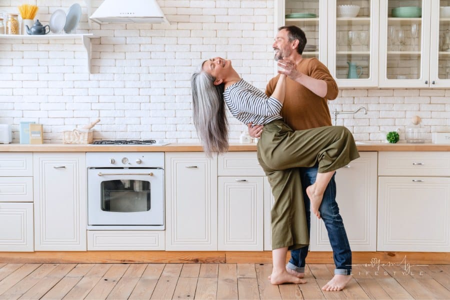 Mature middle-aged couple husband and wife dancing in the kitchen, celebrating date, anniversary.