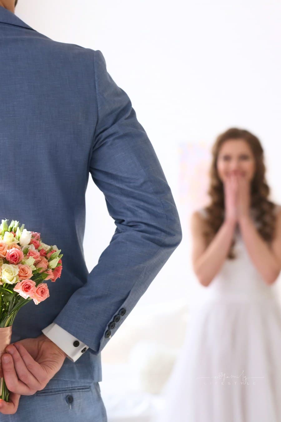 groom holding wedding bouquet behind back with bride excitedly waiting