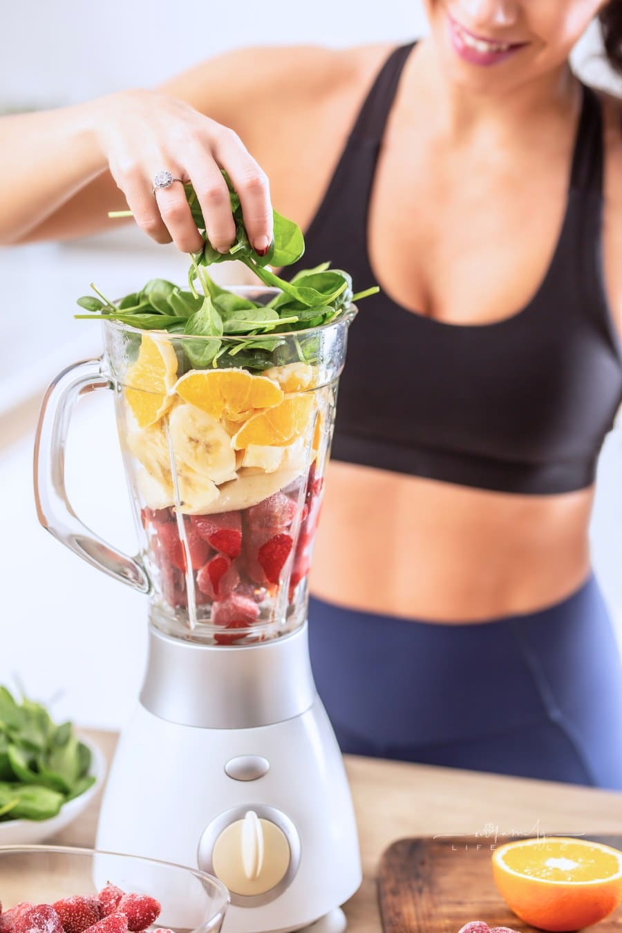 Colorful nutrition of spinach, oranges, bananas and strawberries put into a blender by a fit woman.