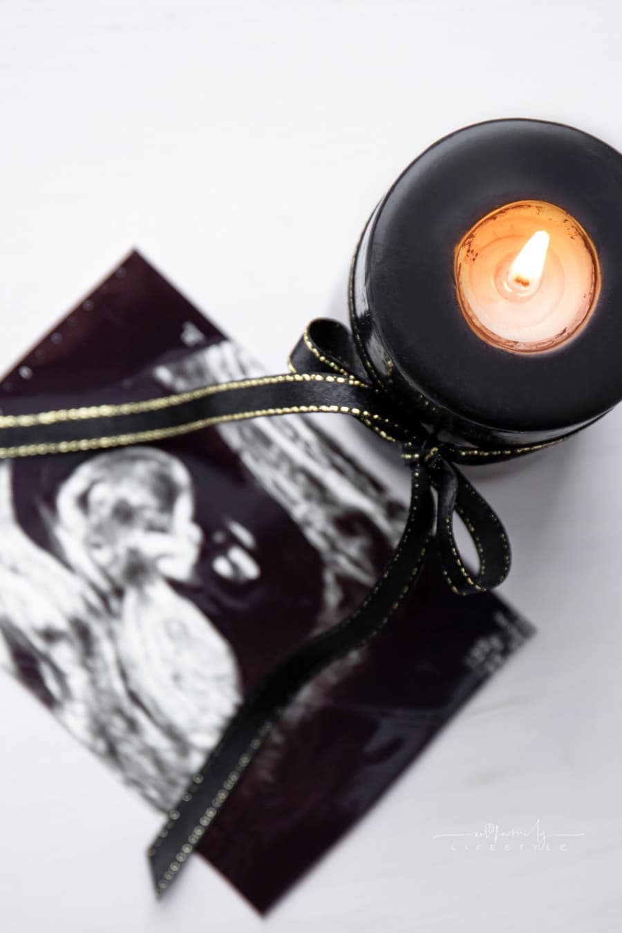 Conceptual image of mourning, miscarriage, pregnancy loss or grief counseling. Ultrasound picture of baby next to black candle with black ribbon burning.