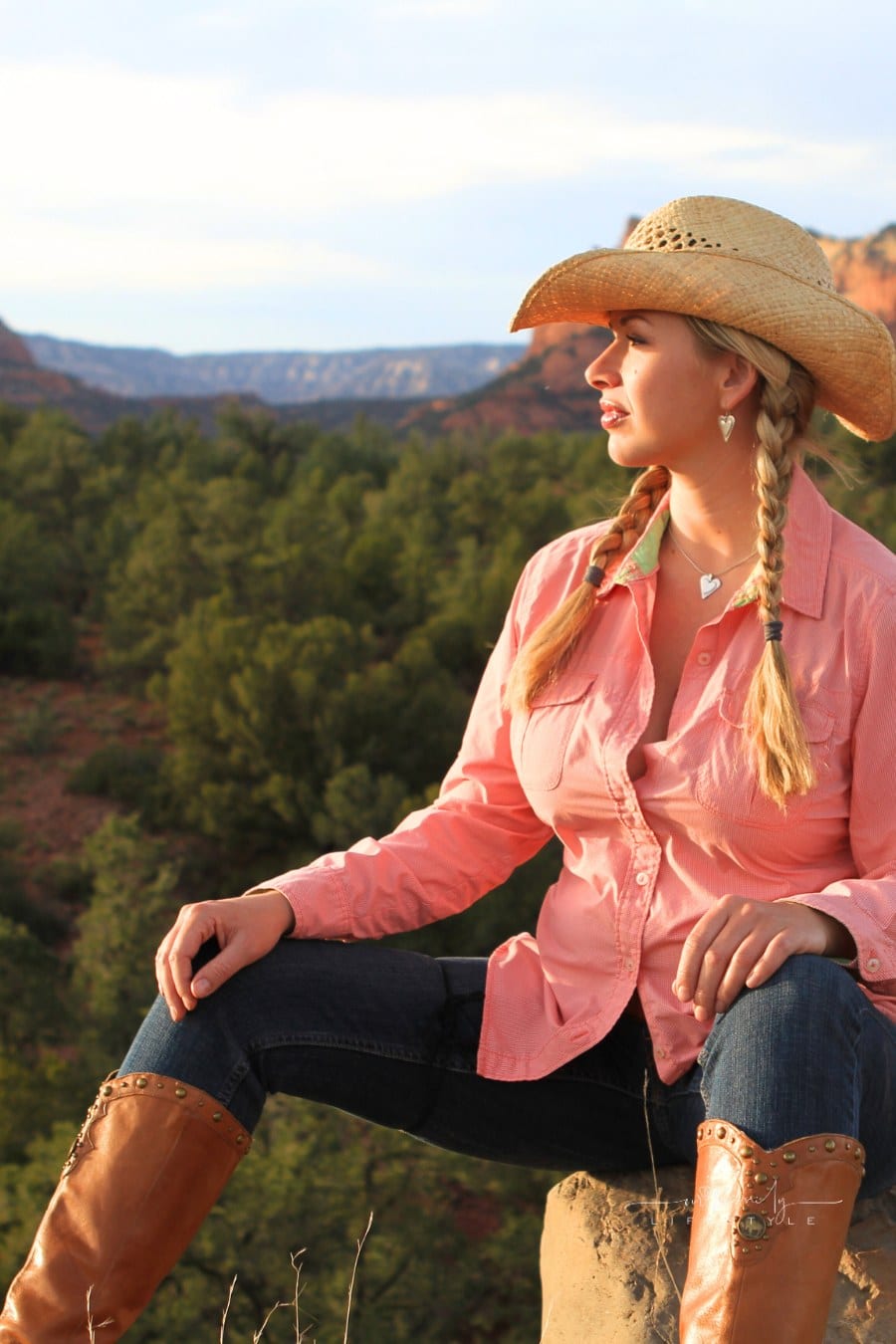Woman with braided blonde hair wearing cowboy boots, pink western shirt, and hat. Shot against the red rocks of Sedona, Arizona.