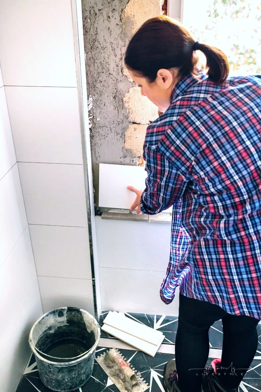 woman laying tile on wall of bathroom