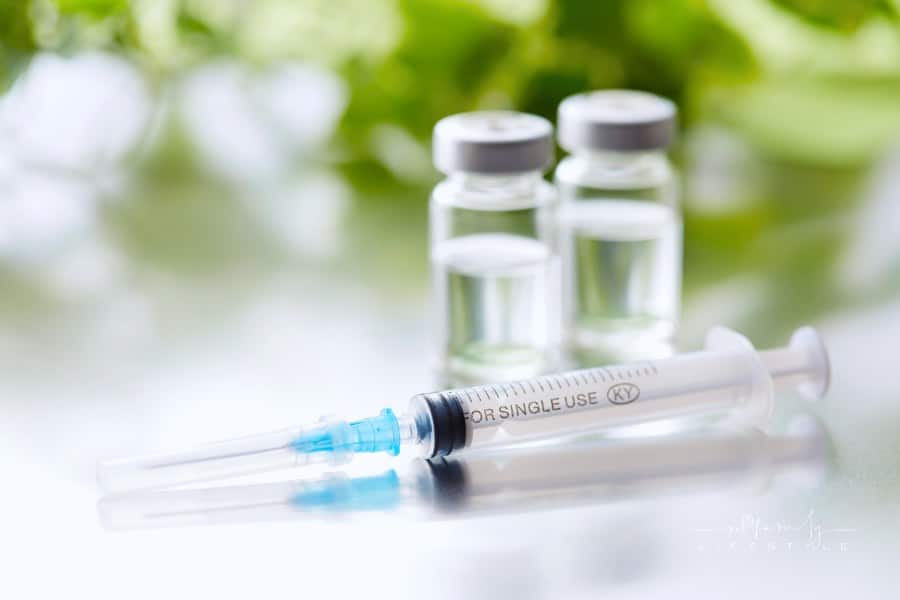 Syringe on Reflective Surface with 2 Vials in Background