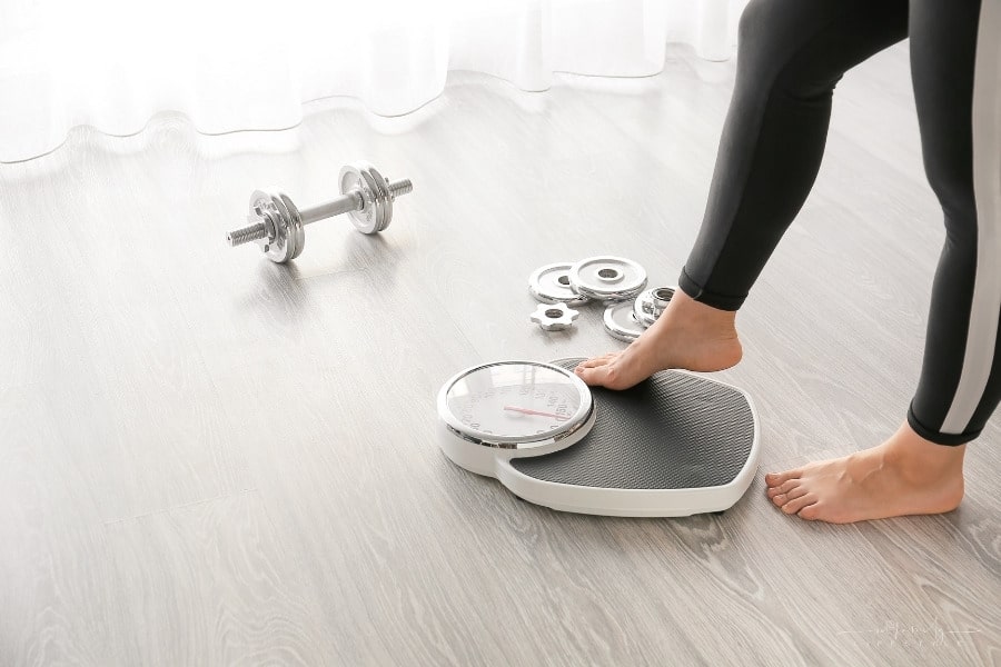 woman stepping on scale with weights and dumbbell nearby