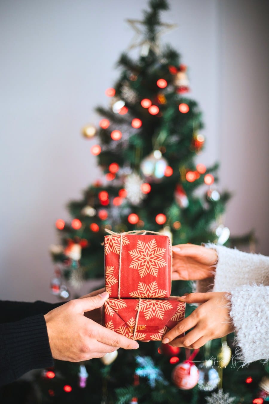 Hands giving gifts in front of a Christmas tree