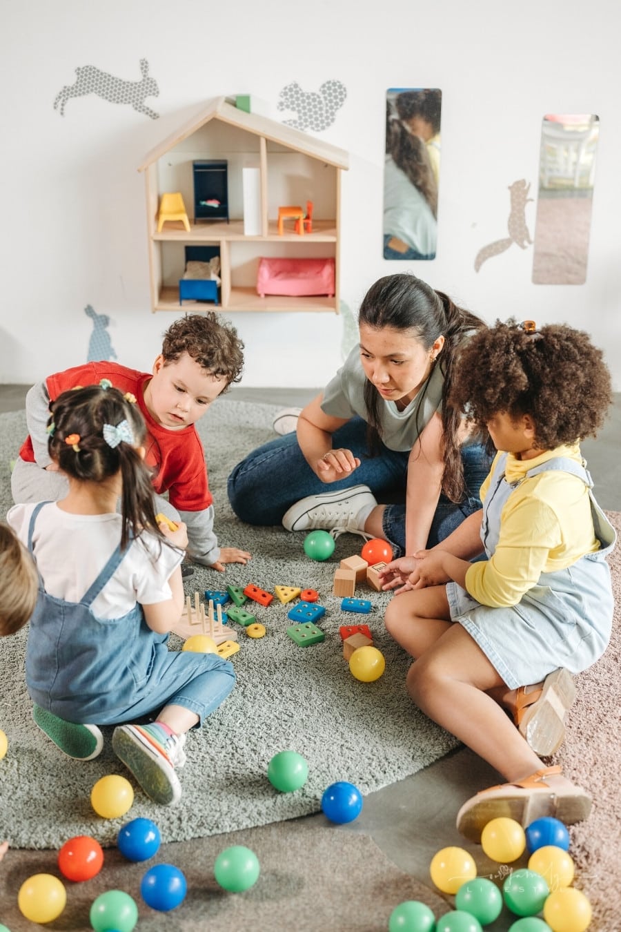 teacher with 3 young students doing a puzzle on floor in preschool