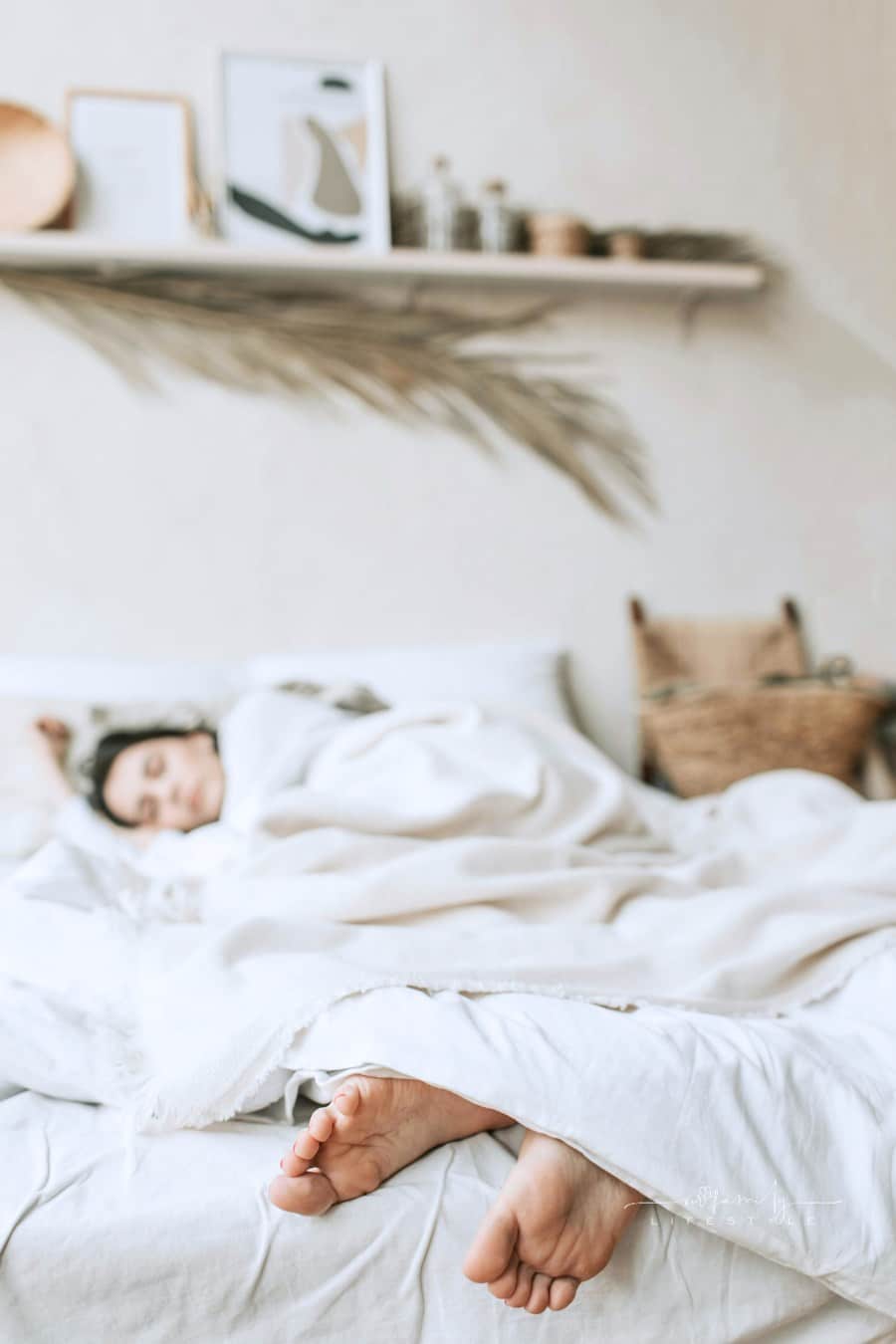 Photo of a Woman Sleeping on a Bed with a White Blanket; feet hanging off end of bed