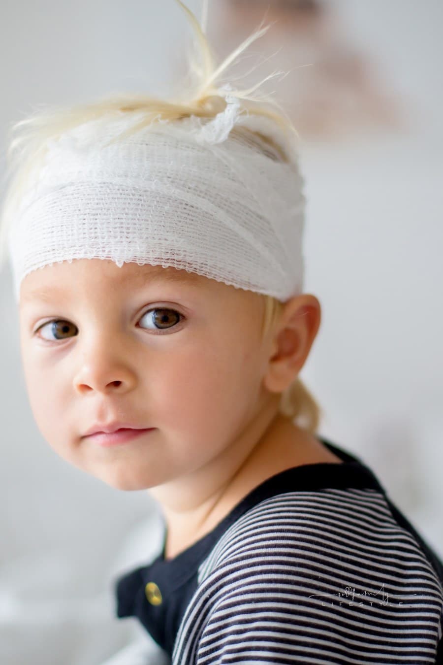 Close portrait of little toddler boy with head injury, sitting in bed, tired, looking at camera