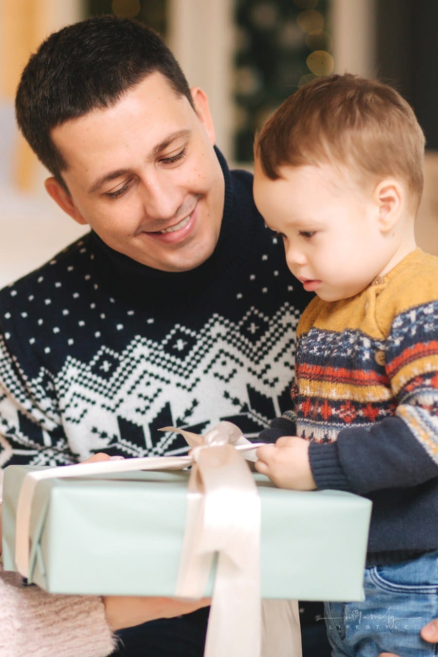 man giving a wrapped gift to toddler boy in sweater