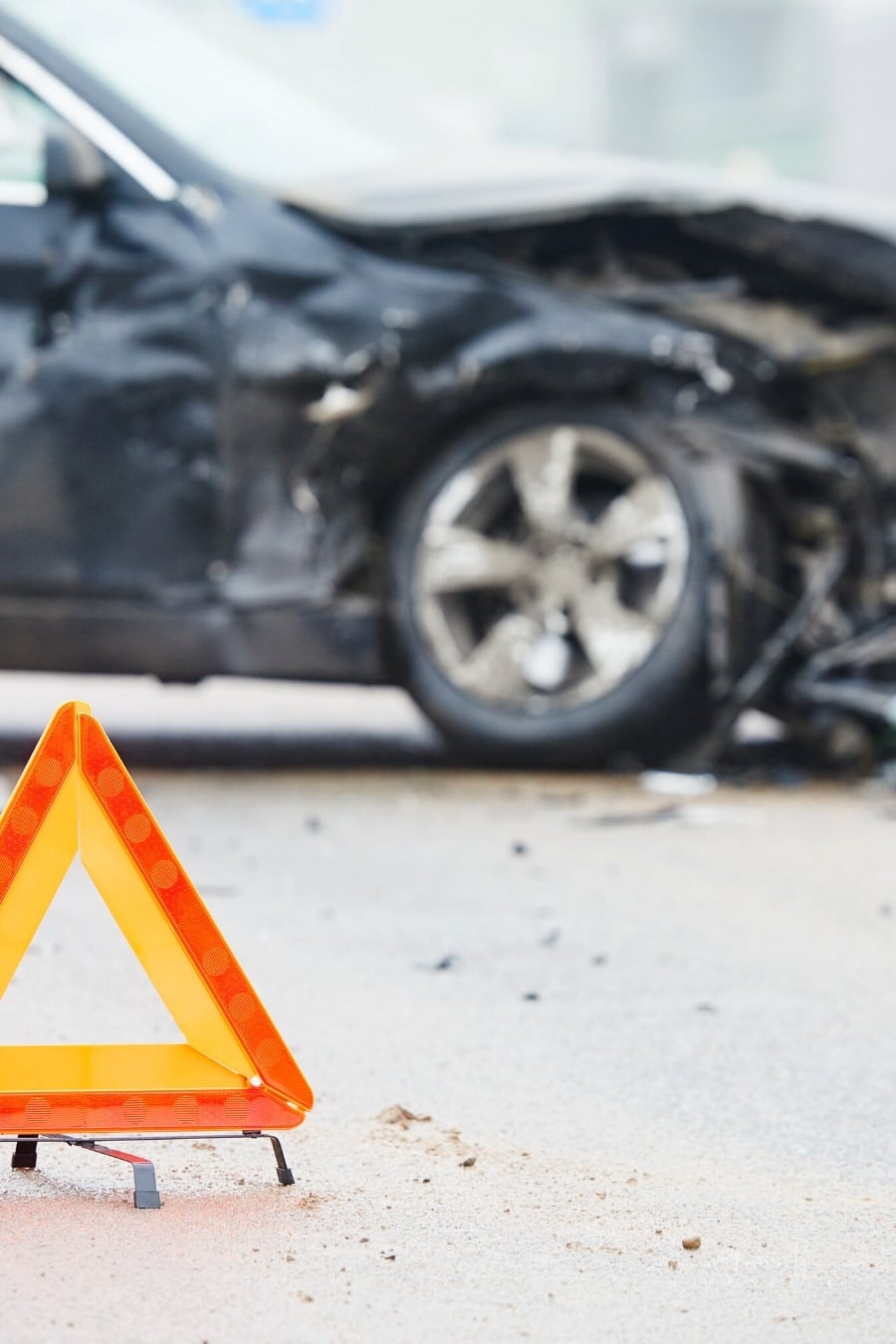 emergency orange hazard triangle in front of a damaged black car after accident