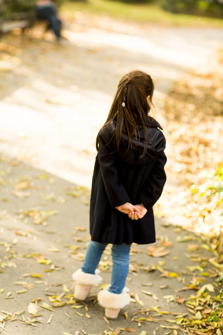 girl walking through park with jacket, jeans, and boots in fall