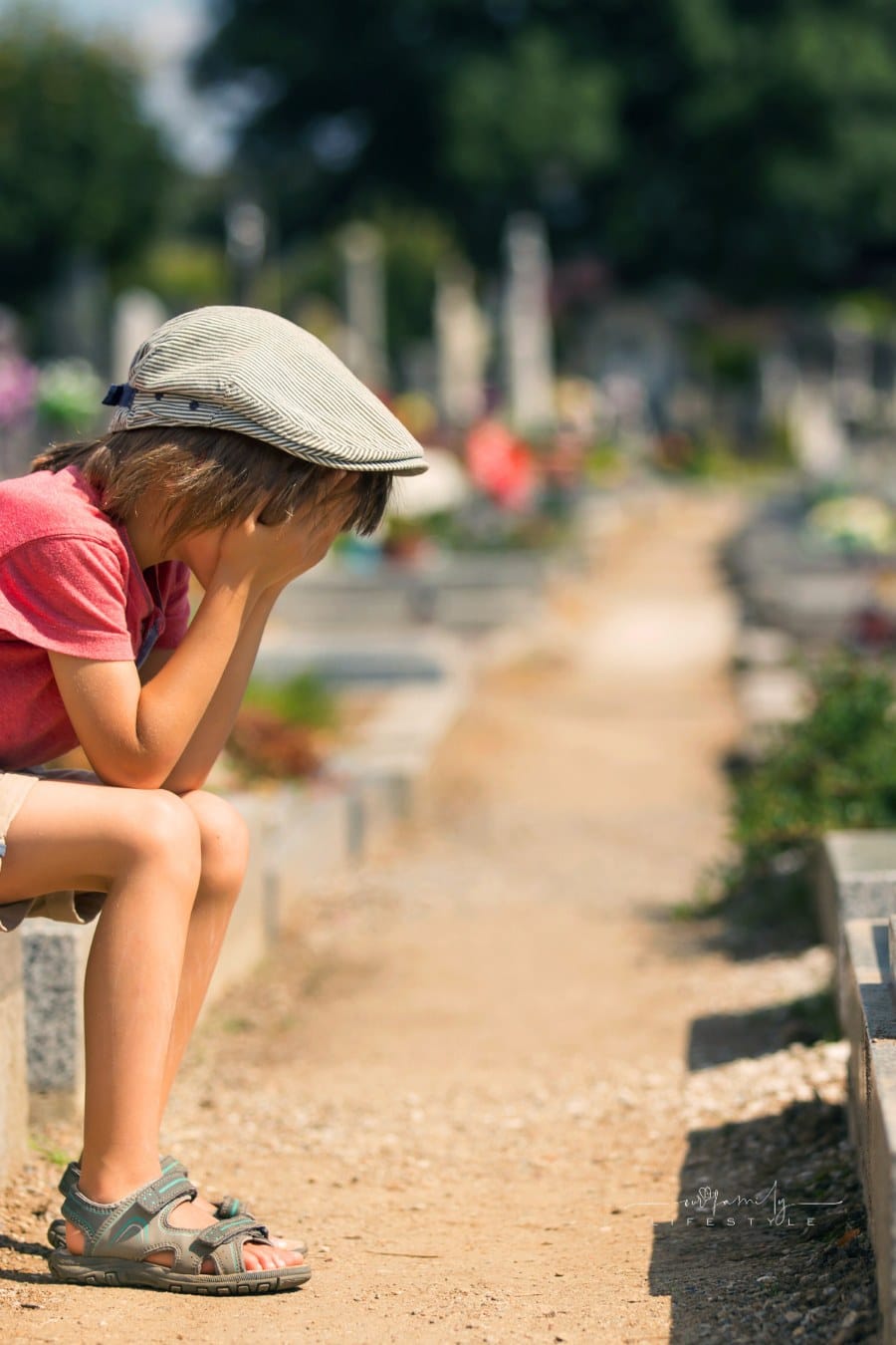 Sad little boy, sitting on a grave in a cemetery, feeling sad and crying