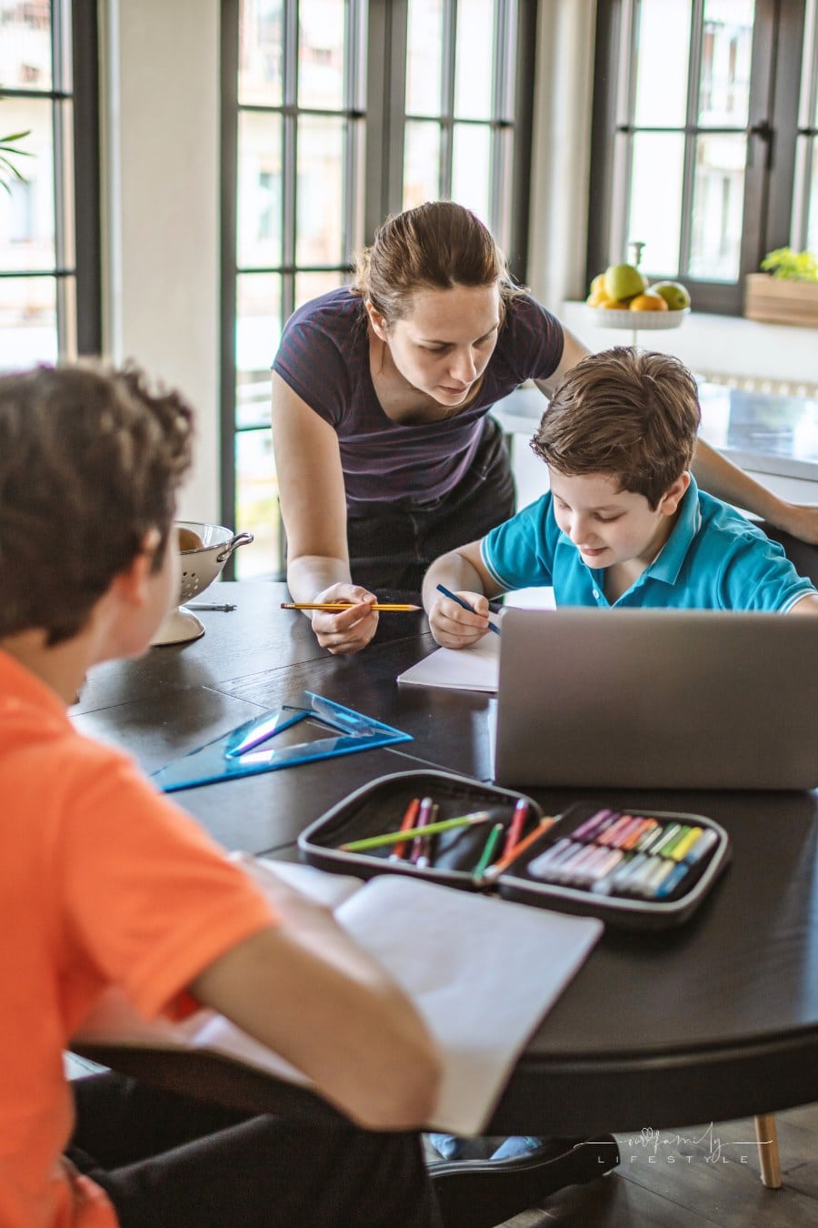 Mother homeschooling boys from home on a dinner table.