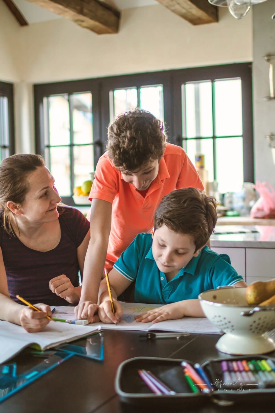 Mother homeschooling boys from home on a dinner table.