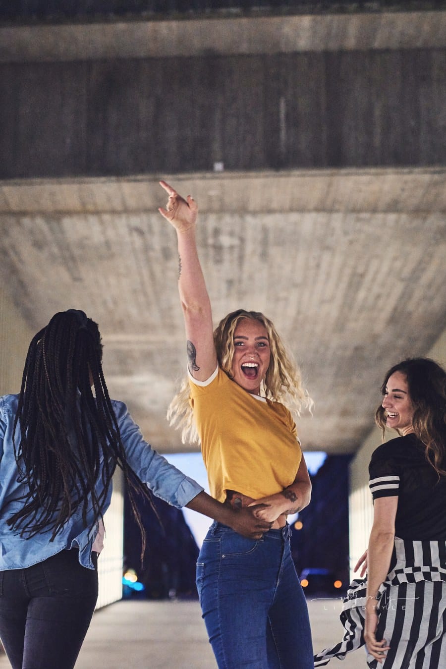 three confident young women walking together; middle woman turning around, smiling, with finger in the air