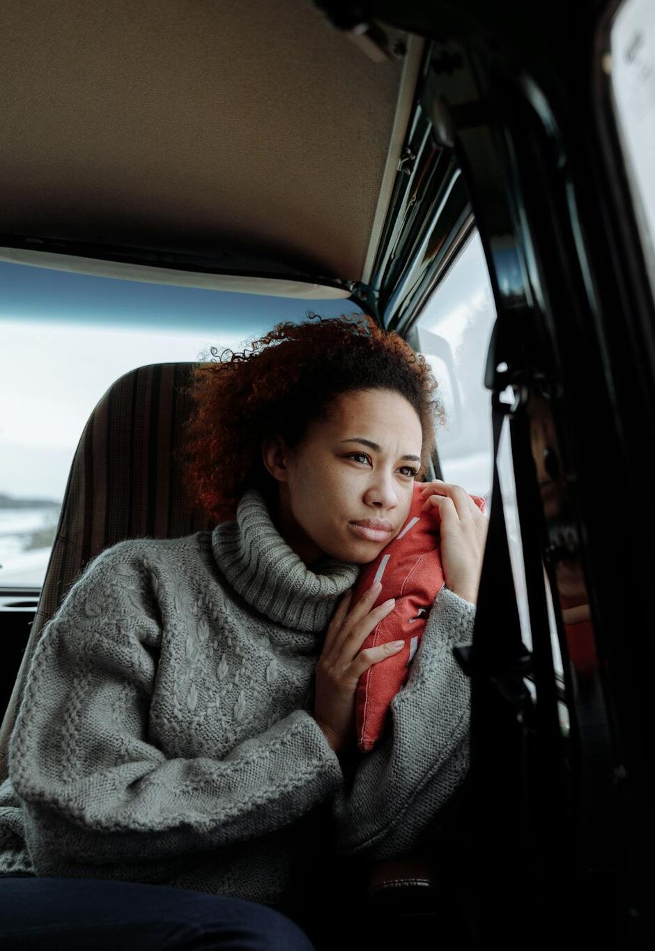 Woman in gray sweater looks out van window at snowy landscape during a winter road trip.