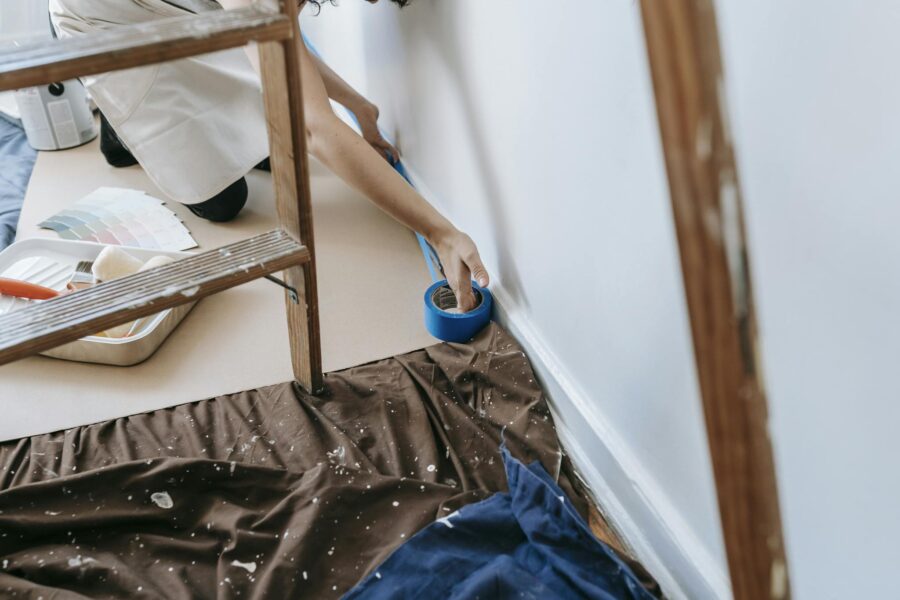 Woman preparing room for painting with adhesive tape and tools; home renovation project.