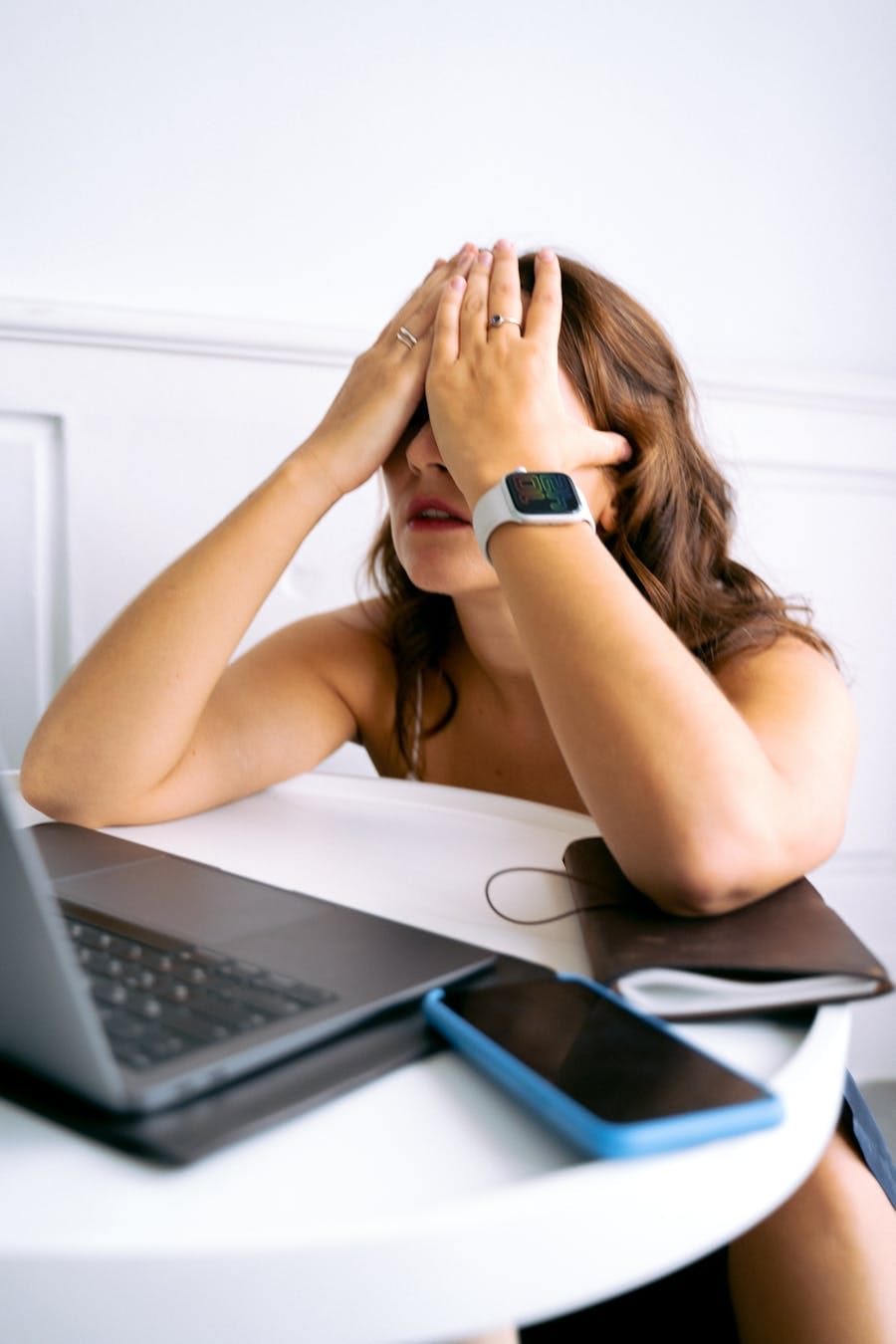 Woman showing stress or tiredness with hands on face at a desk with a laptop.