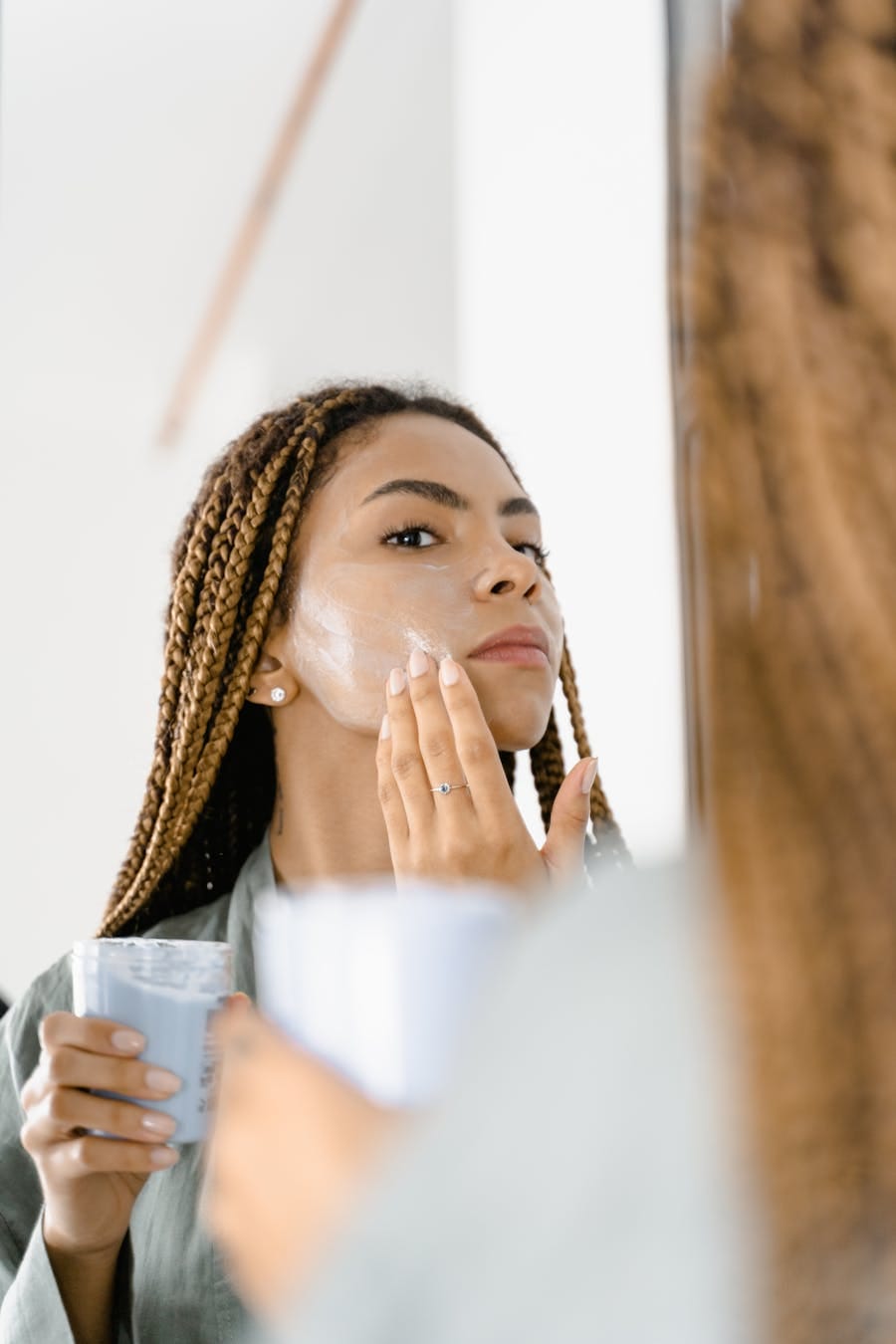 Young woman with braided hair applies facial cream, focusing on self-care and skincare indoors.
