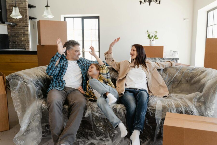 A cheerful family sitting on a couch amidst moving boxes, celebrating their new home.