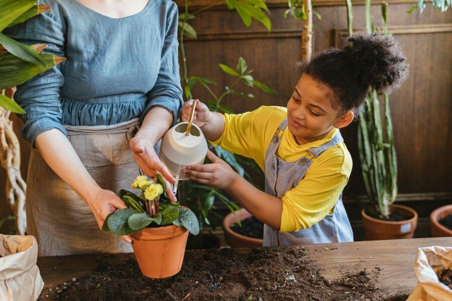 A child and adult watering plants together in an indoor garden setting, promoting bonding and nature.