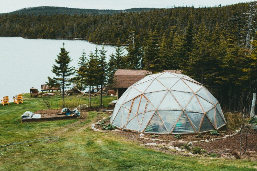 A geodesic dome in a lush forest setting, beside a serene lakeshore, offering a tranquil retreat vibe.