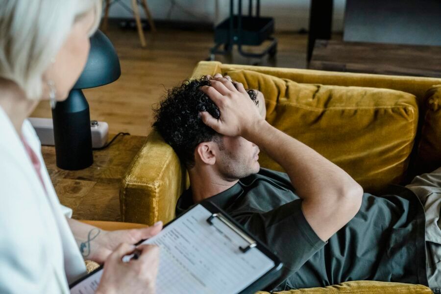A man lying on a sofa during a therapy session, appearing distressed.