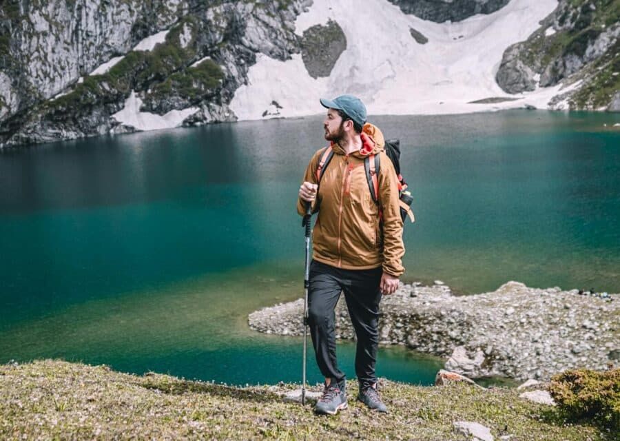 A man stands by a pristine mountain lake surrounded by snow-capped peaks, depicting a serene travel moment.