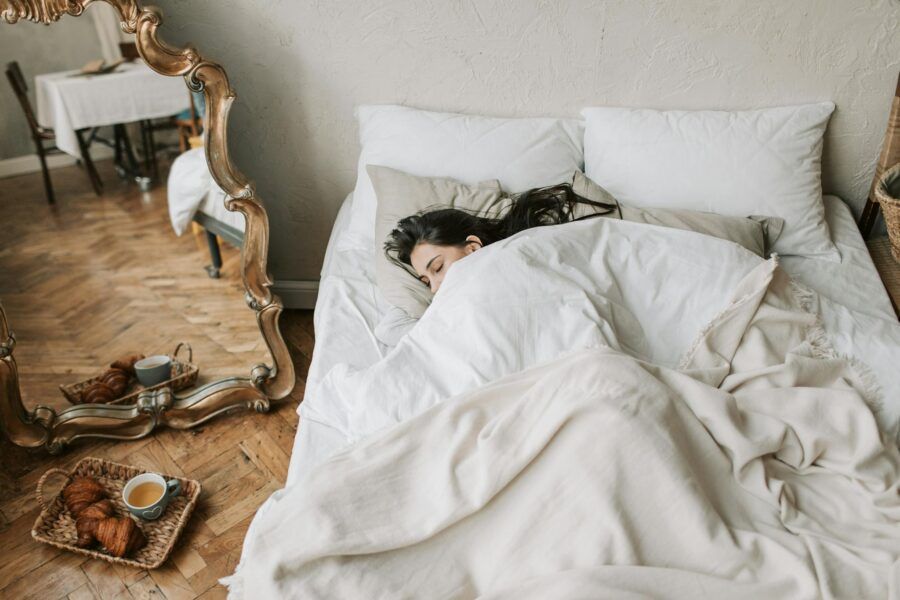 A woman peacefully sleeping in a cozy bed with croissants on the floor.