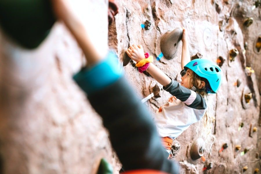 children rock climbing indoors on a large bouldering wall