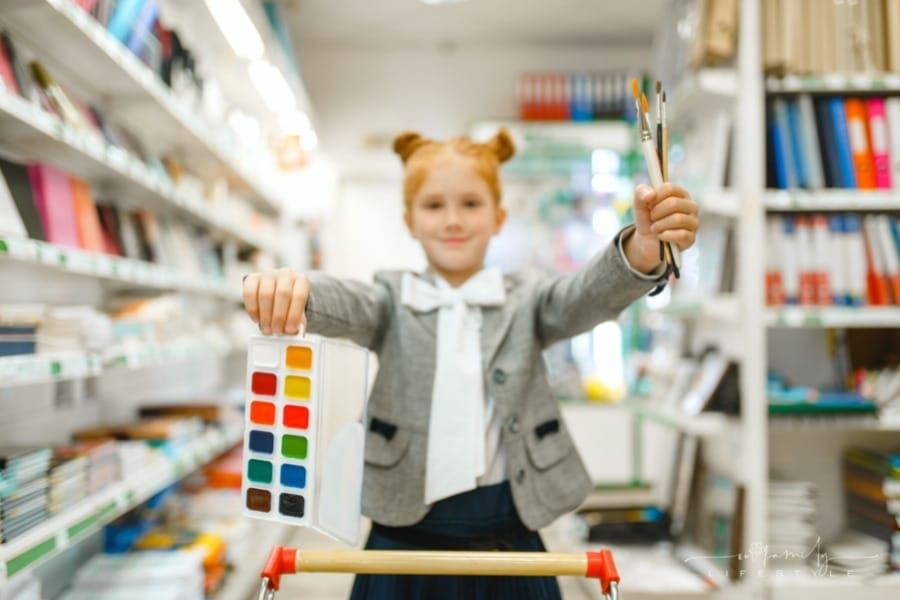 school girl with watercolor paints and brushes in store aisle