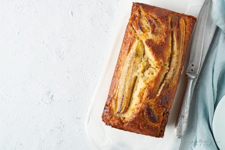 banana bread on a white platter with bread knife nearby for serving