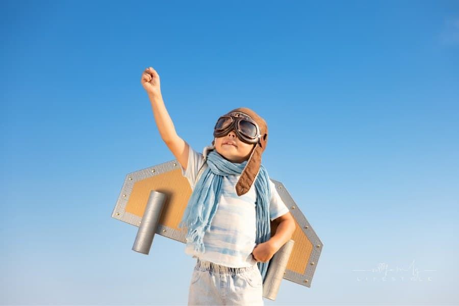 Happy child playing with toy wings against blue sky background. Kid having fun outdoor in summer. Imagination and children dr