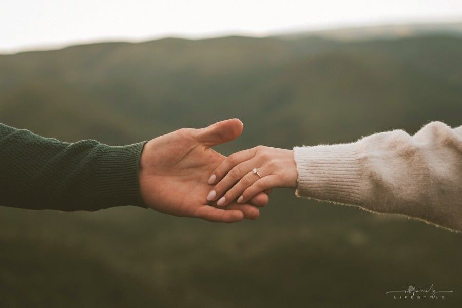 couple holding hands across mountain background with woman wearing engagement ring