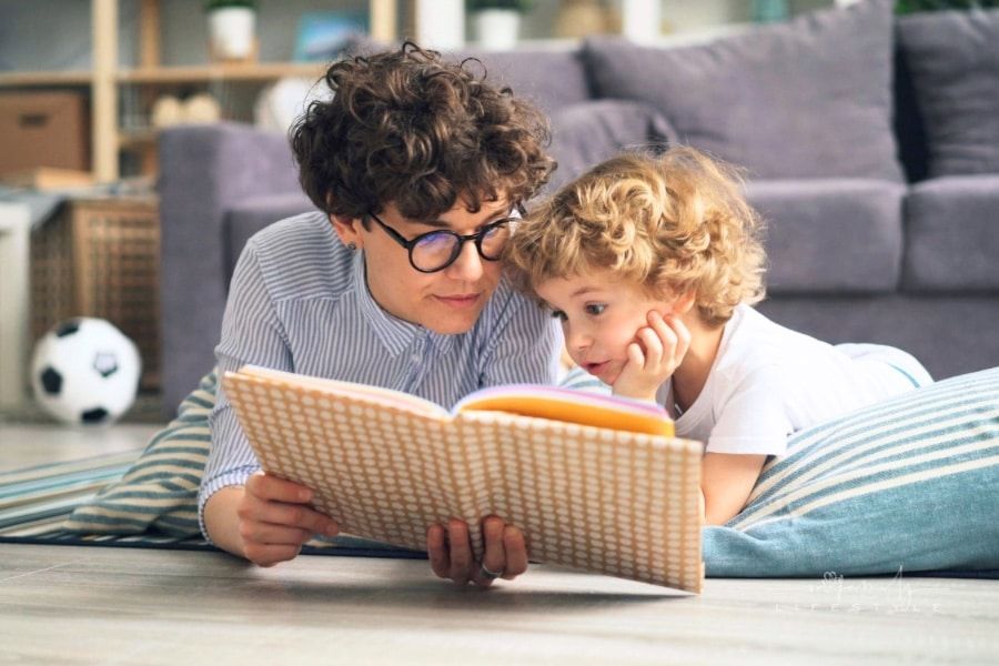 Mom and young son laying on floor cushion reading a book