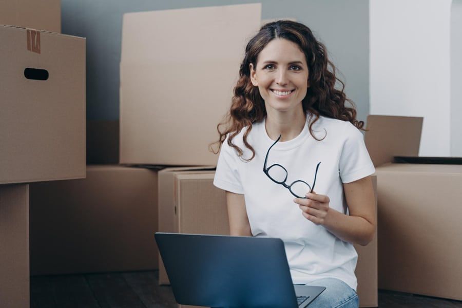 Smiling, moving and storage business owner working on a laptop surrounded by cardboard boxes, showing how local SEO helps mov