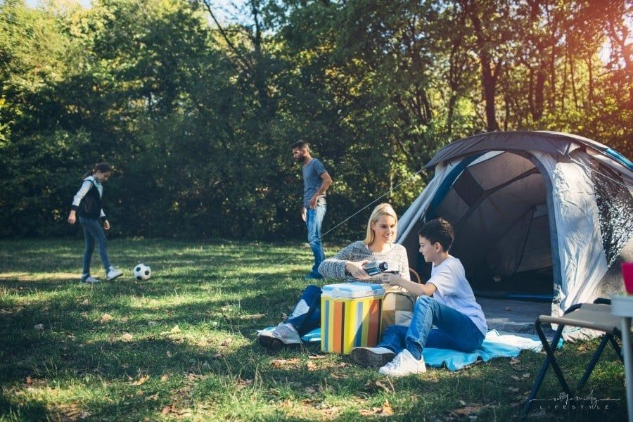 family playing soccer and drinking water while tent camping