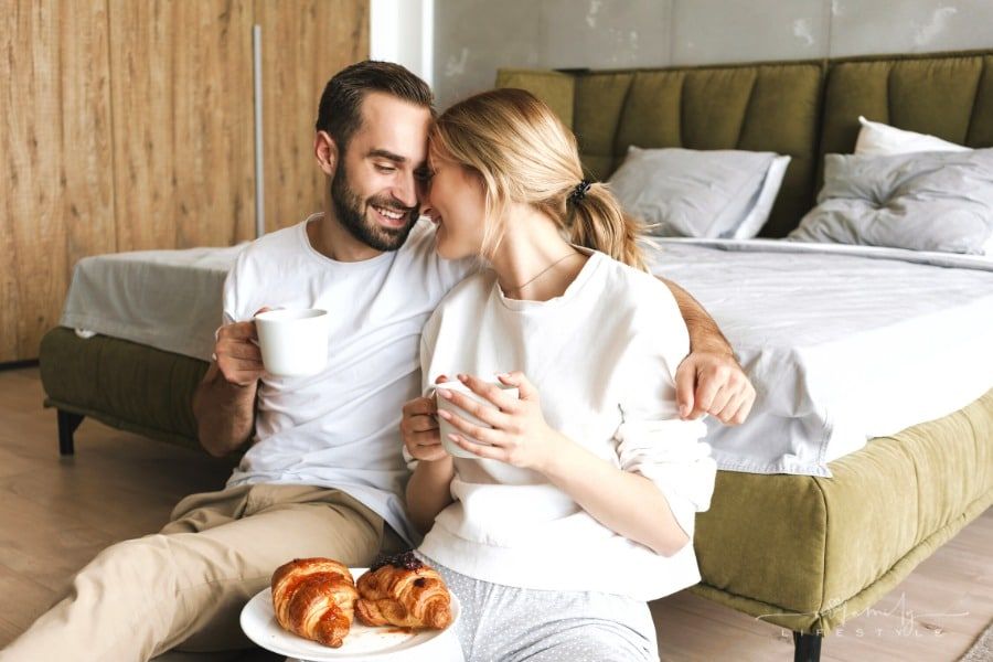 couple drinking coffee and eating croissants at end of bed
