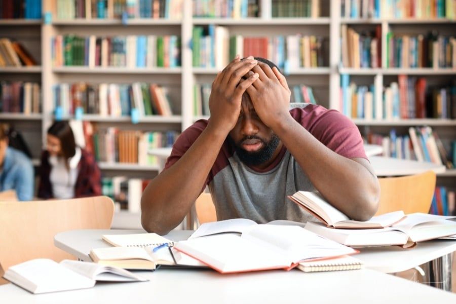 stressed male college student in school library with books open
