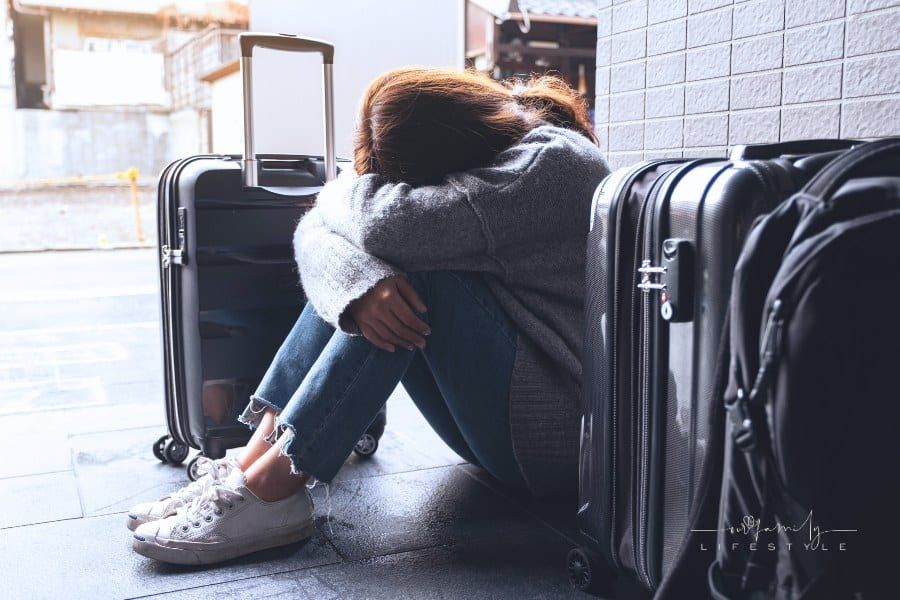A sad, frustrated woman sitting on the floor while traveling with a lot of baggage