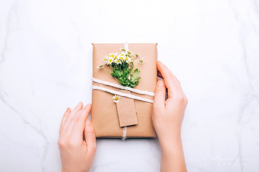 hands holding eco-friendly wrapped gift with recycled paper and real fresh chamomiles