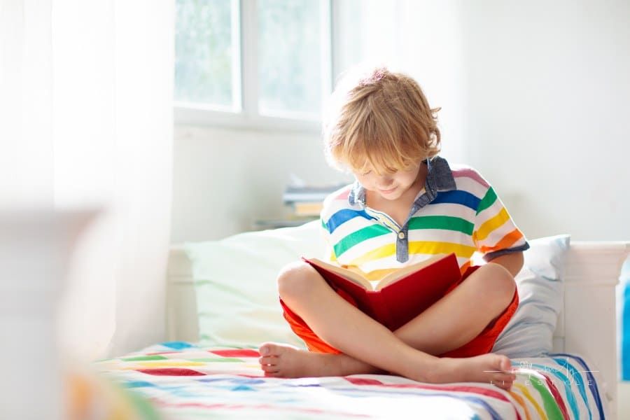 Child reading book in bed. Kids read in bedroom.