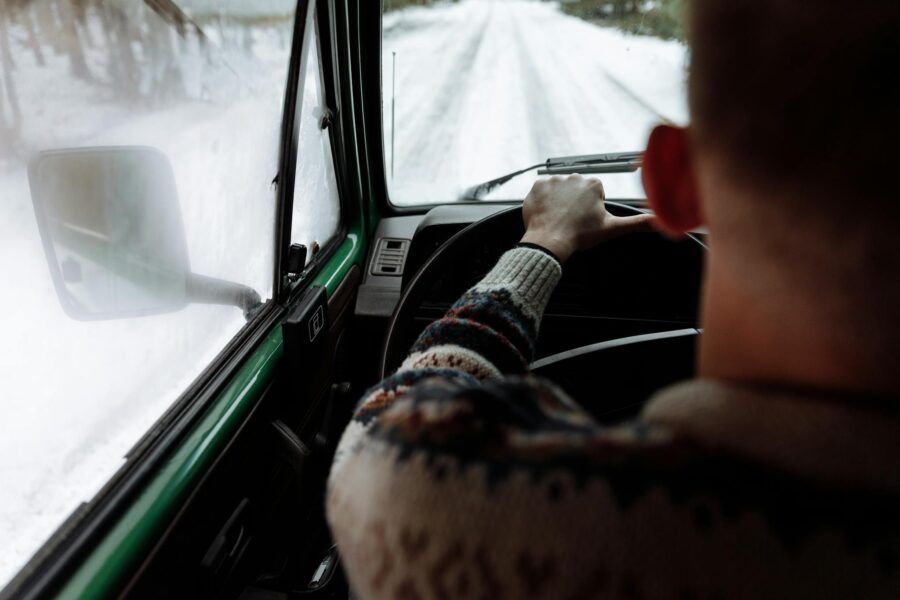 Experience driving on a snowy road with a person in a cozy sweater enjoying the winter view.
