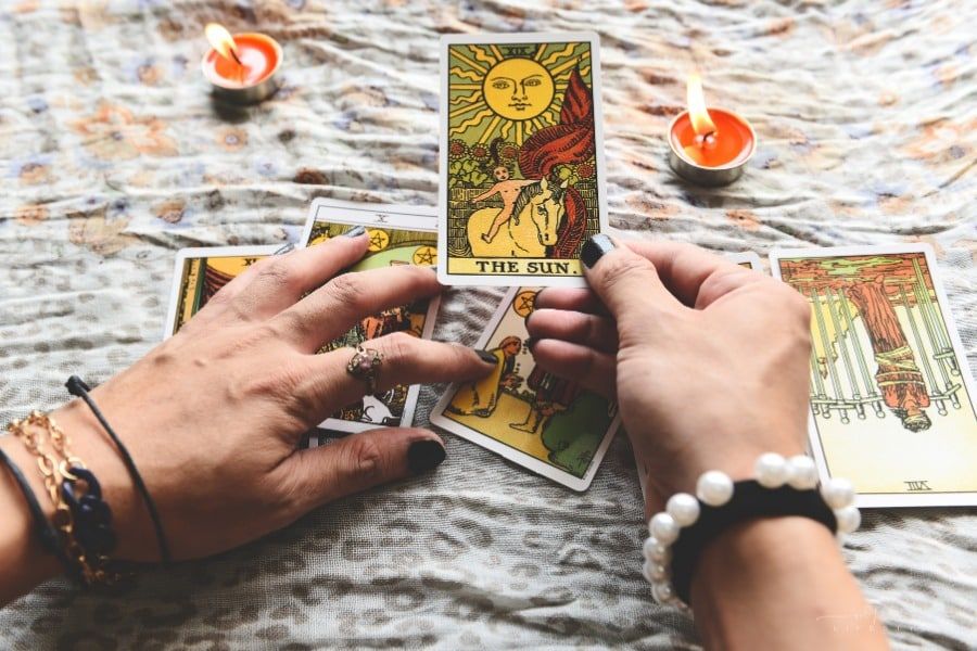 fortune teller's hands holding tarot cards over candellit table