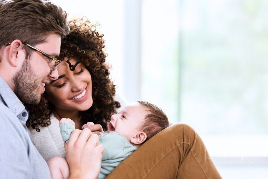 Happy young woman and her husband smile at their sweet newborn baby boy. They are relaxing in their home.