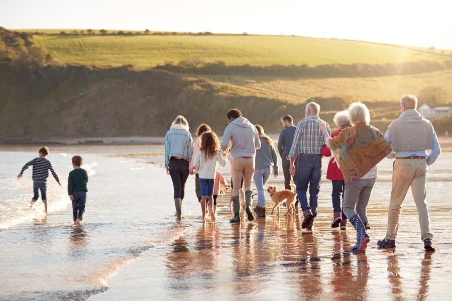 Rear View of Active Multi-Generation Family with Dog Walking Along shore on winter beach vacation