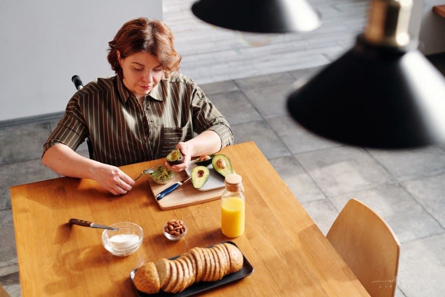 Woman Sitting in wheelchair at dining table while peeling avocados