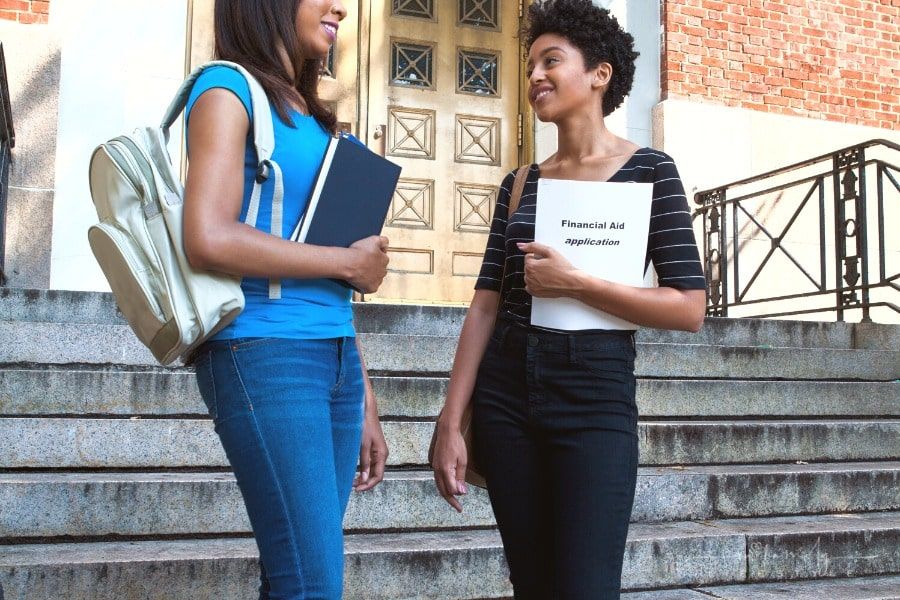 two students standing in front of building entrance with one holding financial aid application