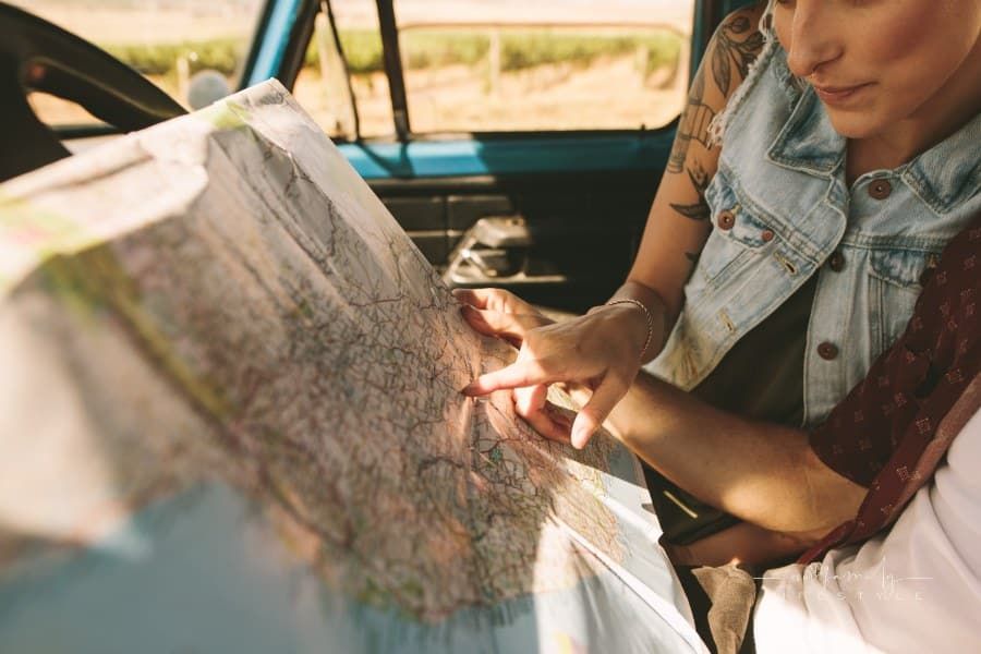 young couple looking at a map sitting in car. Smiling man and woman using map on road trip.