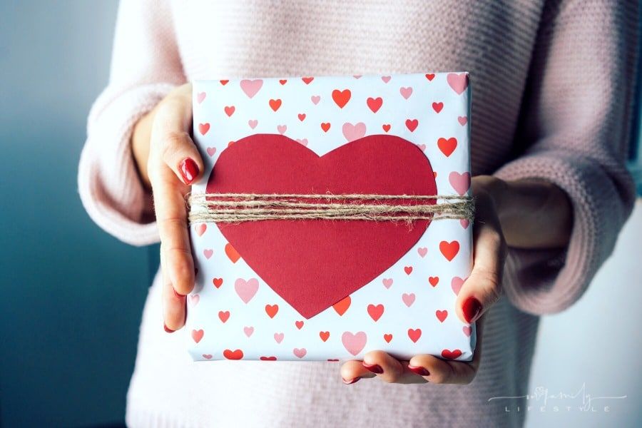 woman holding a gift box decorated with red and pink hearts wrapped in burlap twine